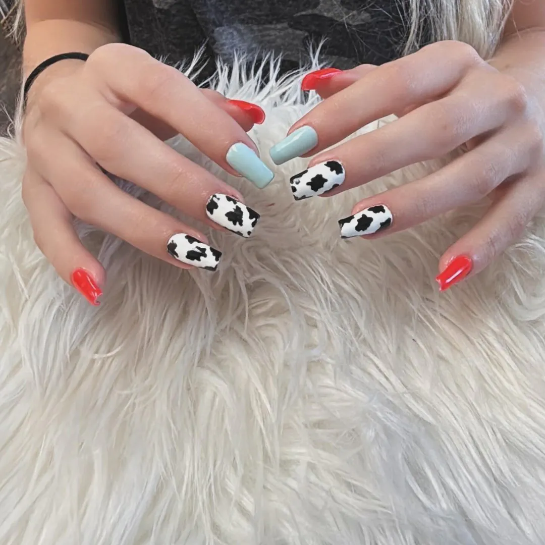 Square nails with black-and-white cow print, mint green and bright red accent nails